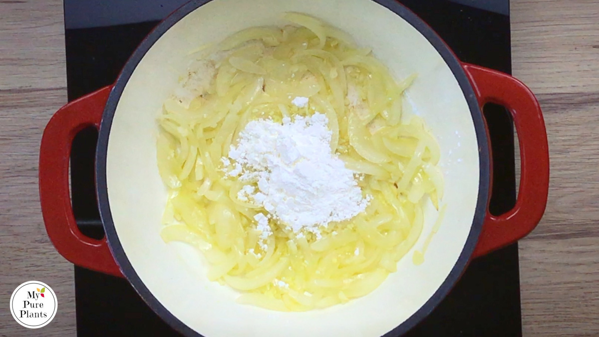 Red-white enameled Dutch oven with lightly cooked sliced onion and garlic, and a small heap of white powder in the middle.