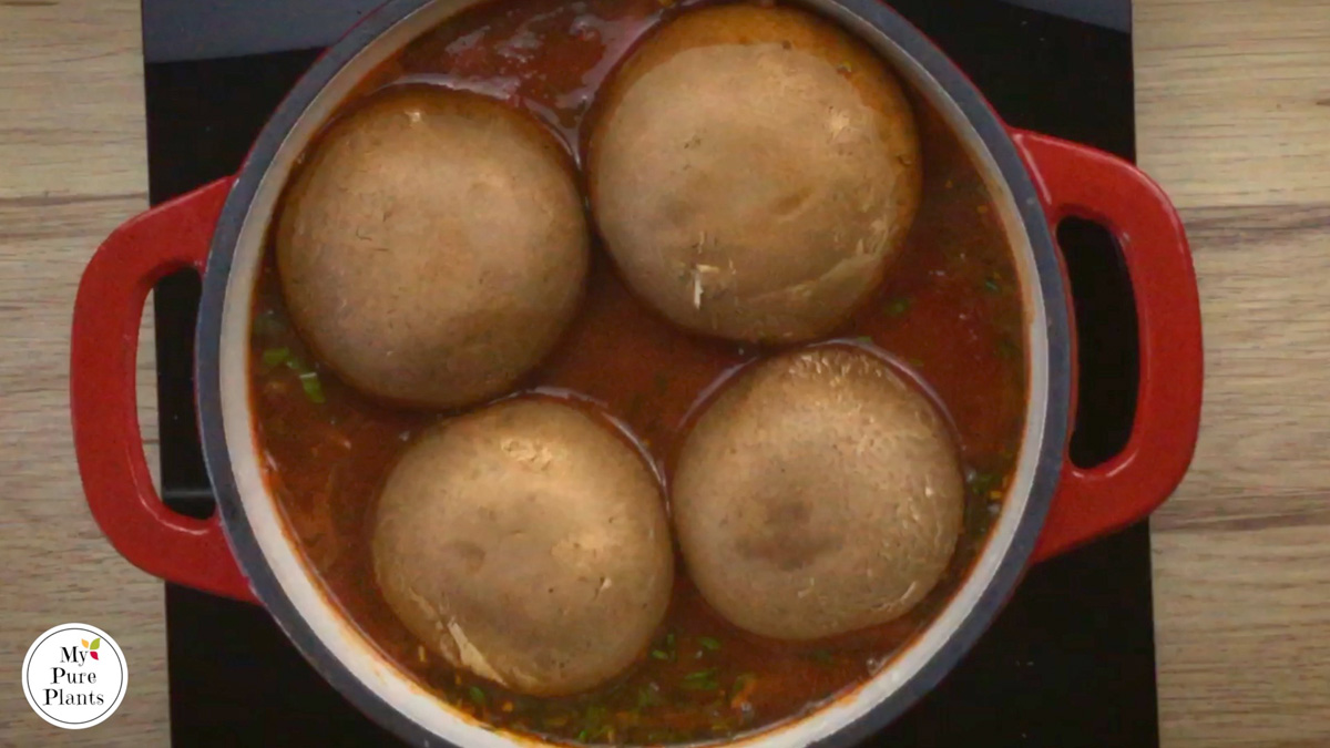 Red-white enameled Dutch oven with a thin red soup and 4 large portobello mushroom caps on top.