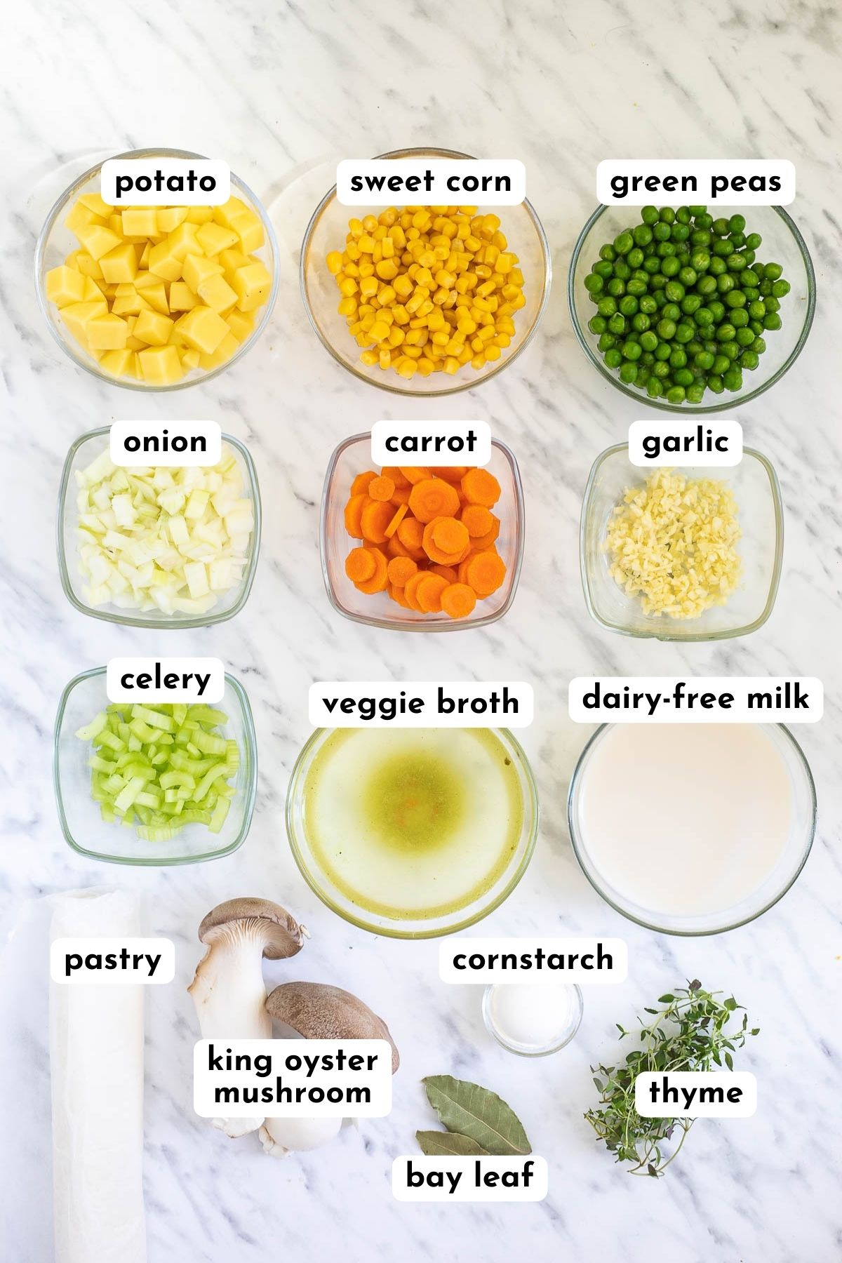 Ingredients of vegan pot pie in small glass bowls like potato, corn, peas, carrots, onion, garlic, celery, milk, broth, puff pastry, king oyster mushrooms, bay leaves, and thyme.