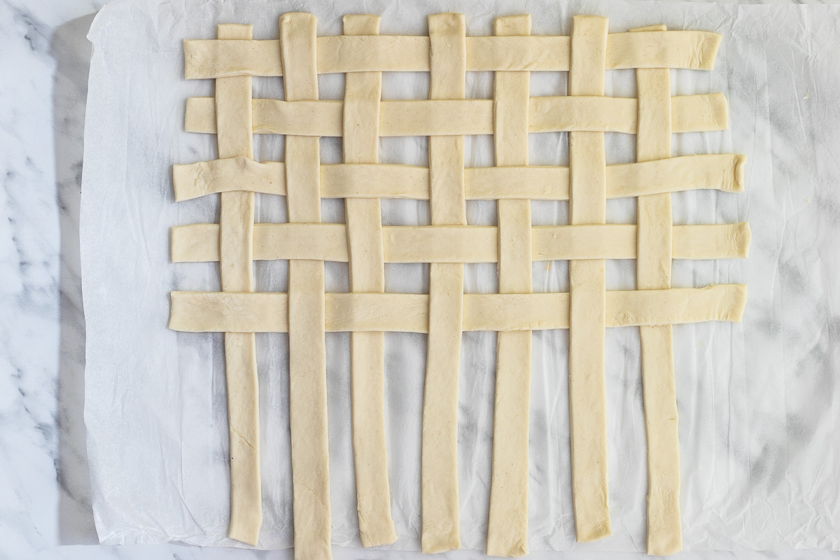 Stripes of puff pastry weaved together on a marble surface.