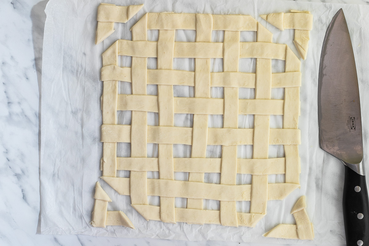 Stripes of puff pastry weaved together on a marble surface. The corners are cut off.