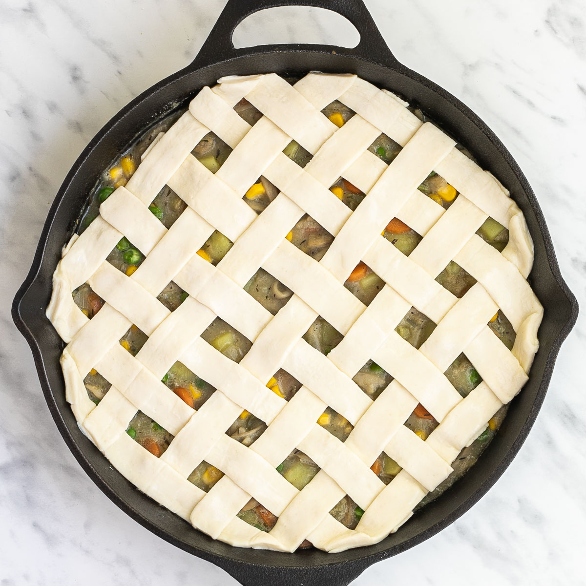 Puff pastry in lattice pattern placed on top of a veggie stew in a cast iron skillet.
