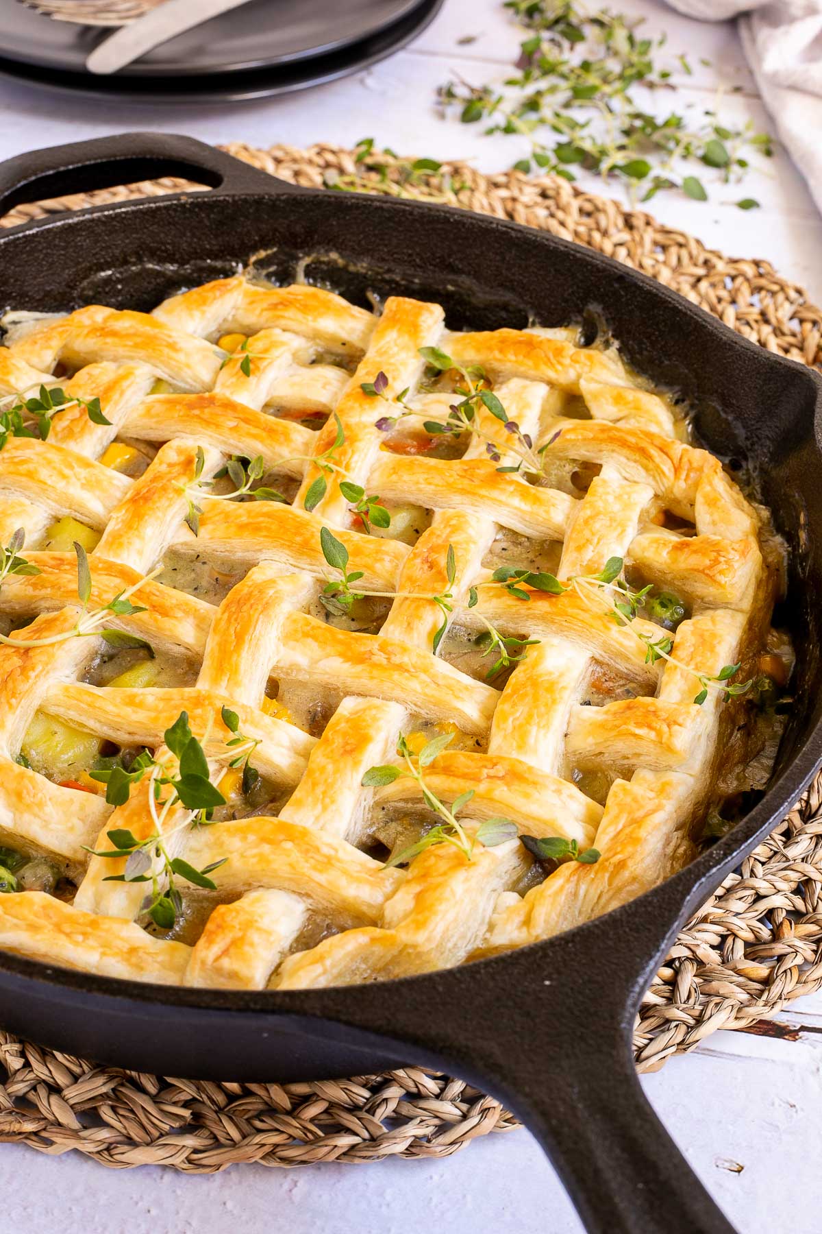 Cast iron skillet with veggie stew topped with puff pastry in a lattice pattern.