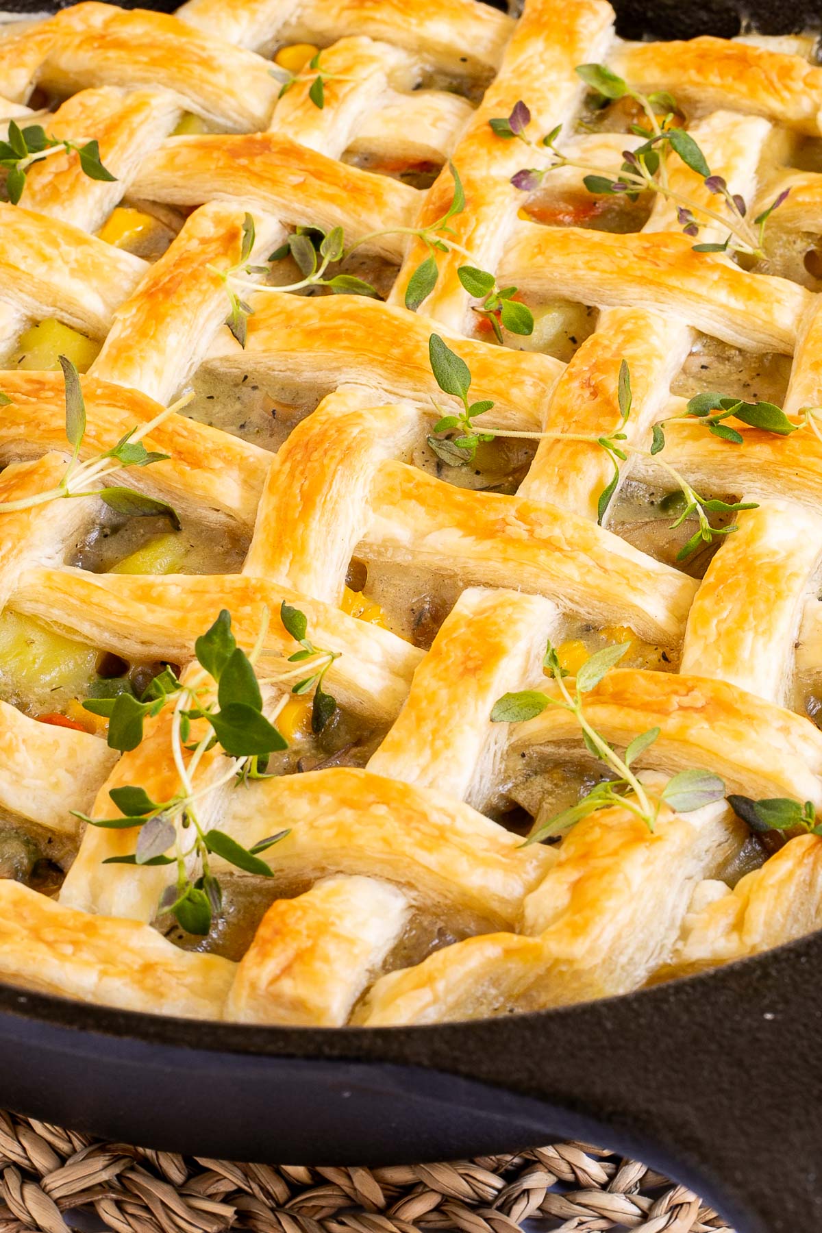 Cast iron skillet with veggie stew topped with puff pastry in a lattice pattern.