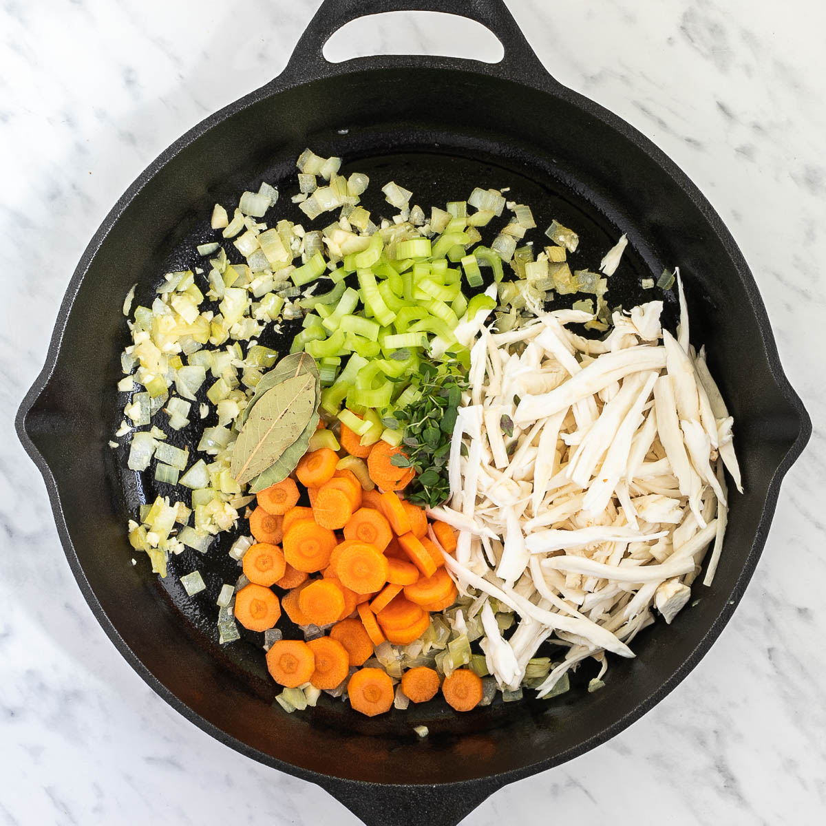 Cast iron skillet with sliced carrots, chopped onion, garlic, celery, shredded king oyster mushrooms, bay leaves, and thyme.