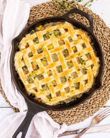 Cast iron skillet with veggie stew topped with puff pastry in a lattice pattern.