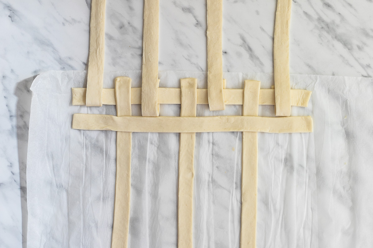 Stripes of puff pastry weaved together on a marble surface.
