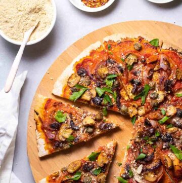 Sliced pizza with red sauce, topped with mushroom, large tomato slices, red onion slices and fresh herbs
