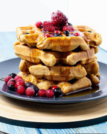 Black plate with a stack of waffles topped with mixed berries and maple syrup