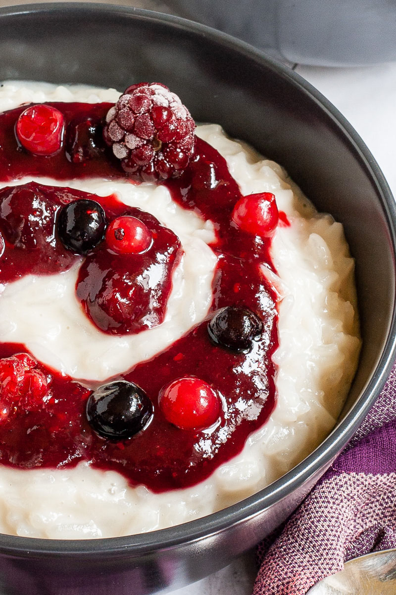 A black bowl up close with white pudding topped with a swirl of thick red-purple sauce and different berries.