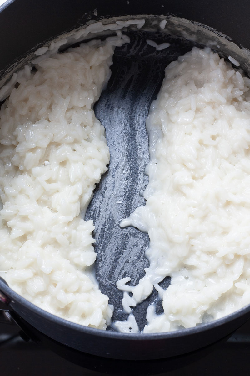 A black saucepan with white creamy rice split in the middle with a draw of a spatula.
