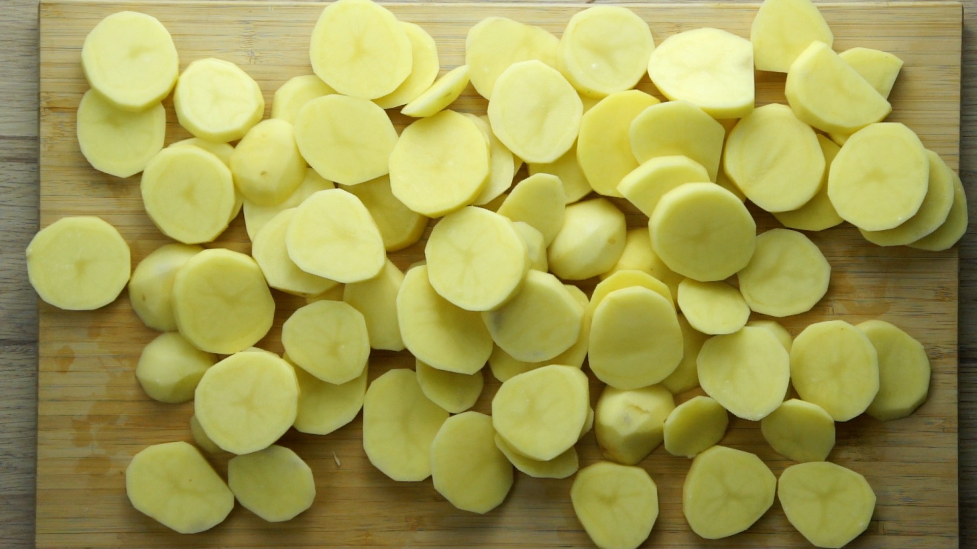 A wooden board full of sliced potatoes
