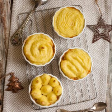 4 white ceramic pots with shepherd's pie from above but only the lovely yellow mashed potato topping is visible.
