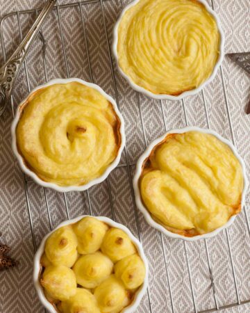 4 white ceramic pots with shepherd's pie from above but only the lovely yellow mashed potato topping is visible.