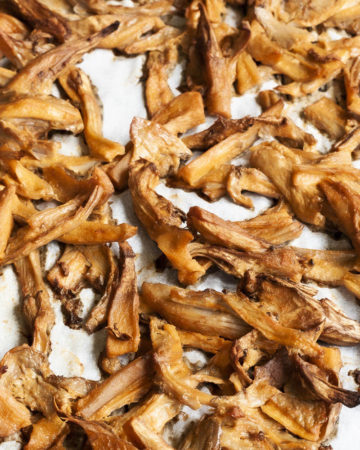Shredded mushrooms scattered around a white parchment paper