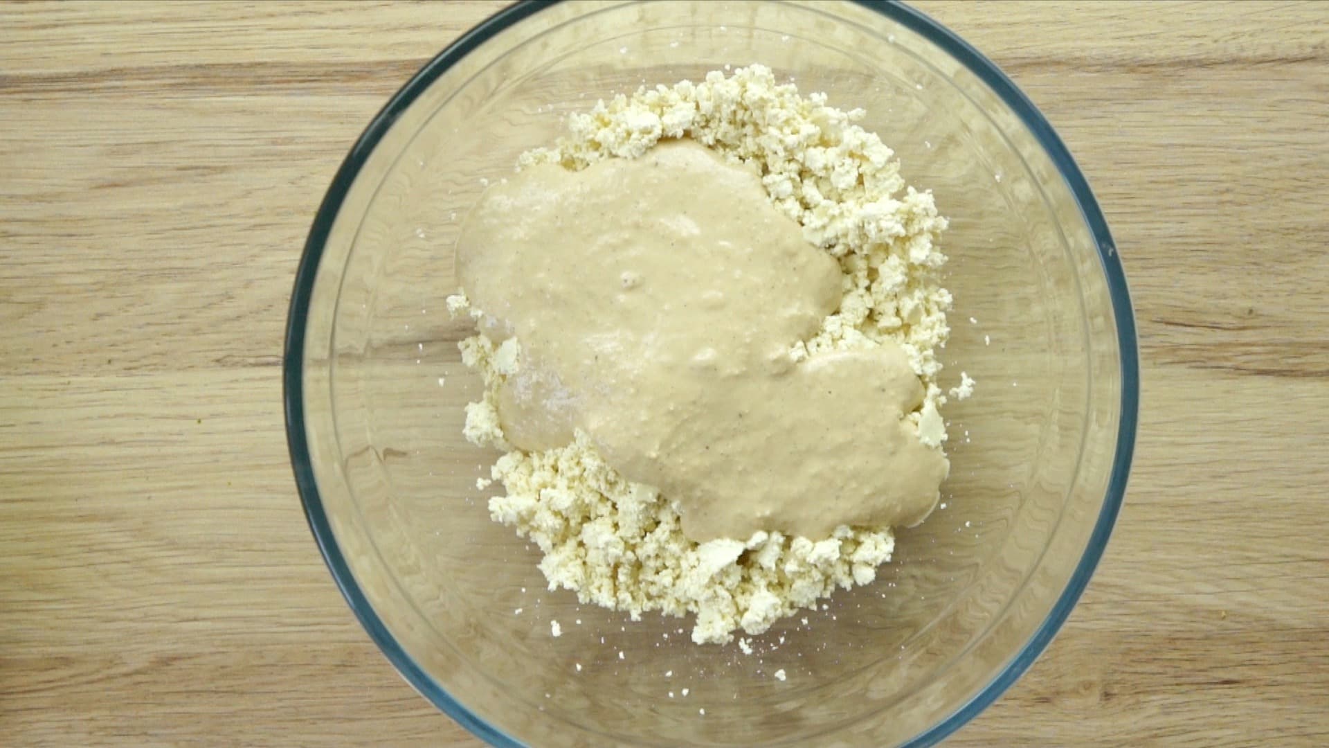 Crumbled tofu in a glass mixing bowl covered with a thick light brown sauce.