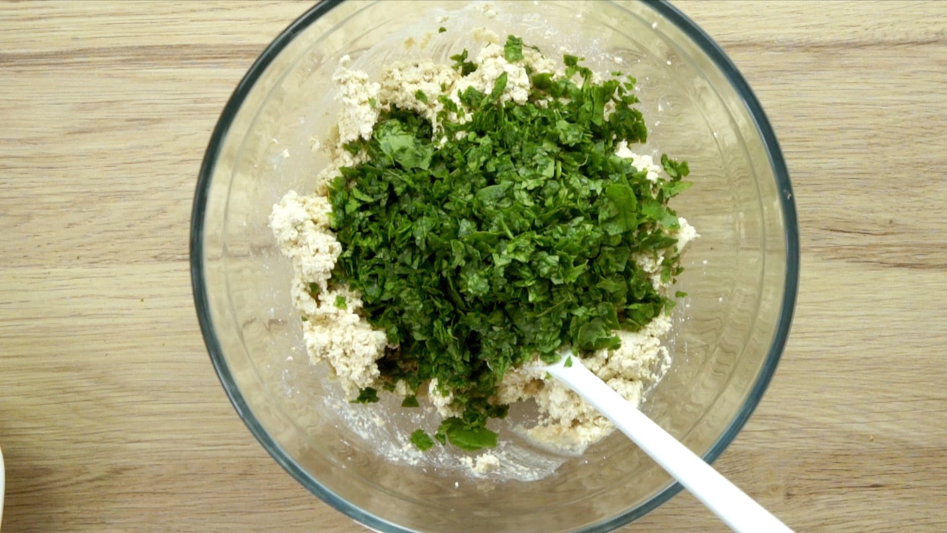 Crumbled tofu in a glass mixing bowl covered with finely chopped spinach leaves.