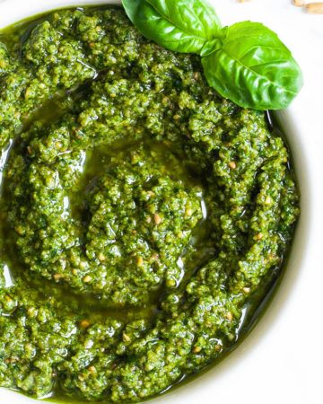 Small white bowl with a chunky green paste and a fresh basil leaf on the side.