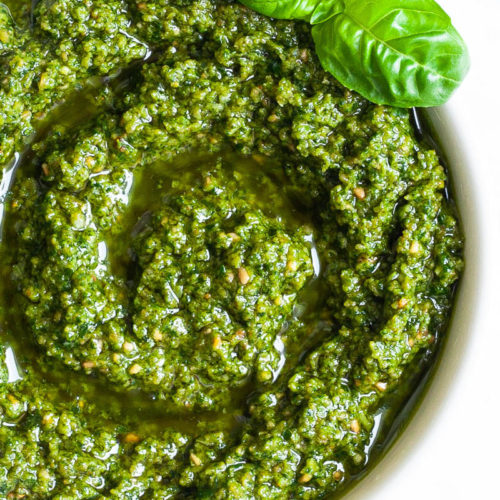 Small white bowl with a chunky green paste and a fresh basil leaf on the side.