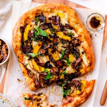 Pizza topped with butternut squash slices, dark brown bacon-like pieces and fresh chopped basil.
