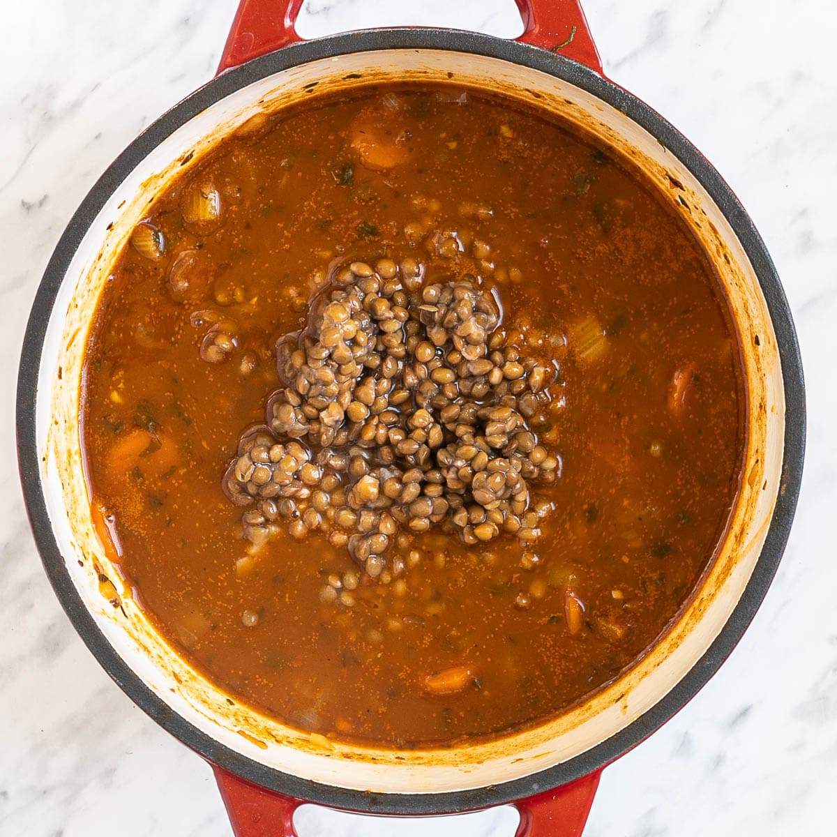 A red-white Dutch oven with dark brown thick stew and lentils.