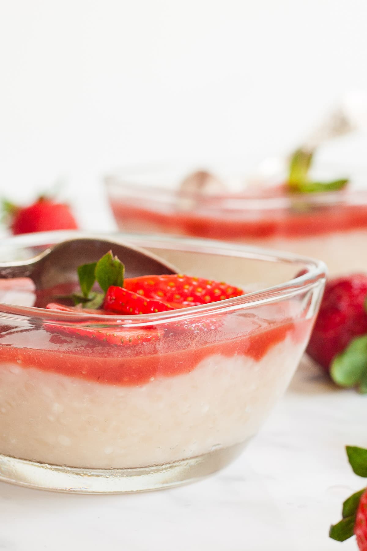 2 small glass bowls with white pudding with pearls topped with strawberry sauce and fresh strawberry slices.