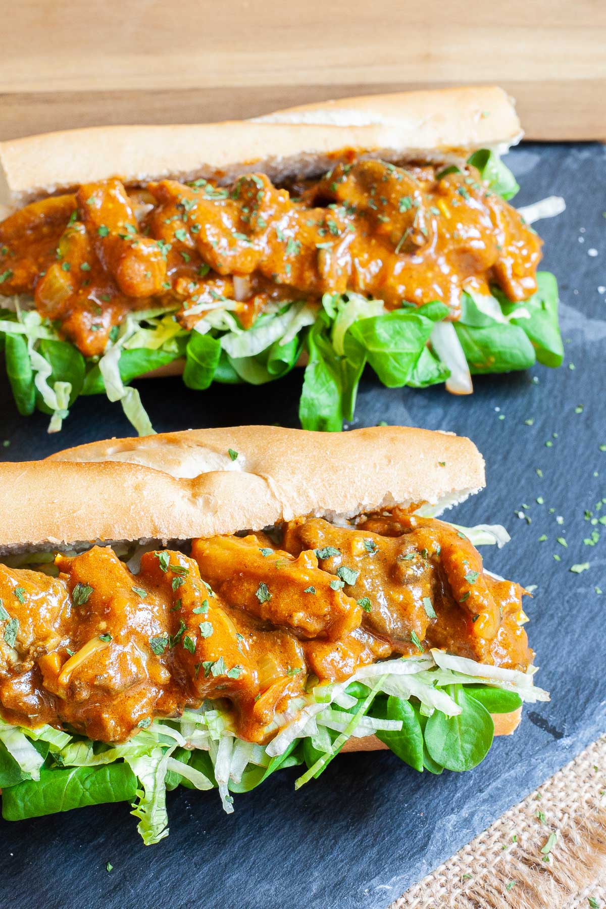 2 hoagie rolls with chopped lettuce and arugula topped with mushroom strips in a brown orange juicy sauce