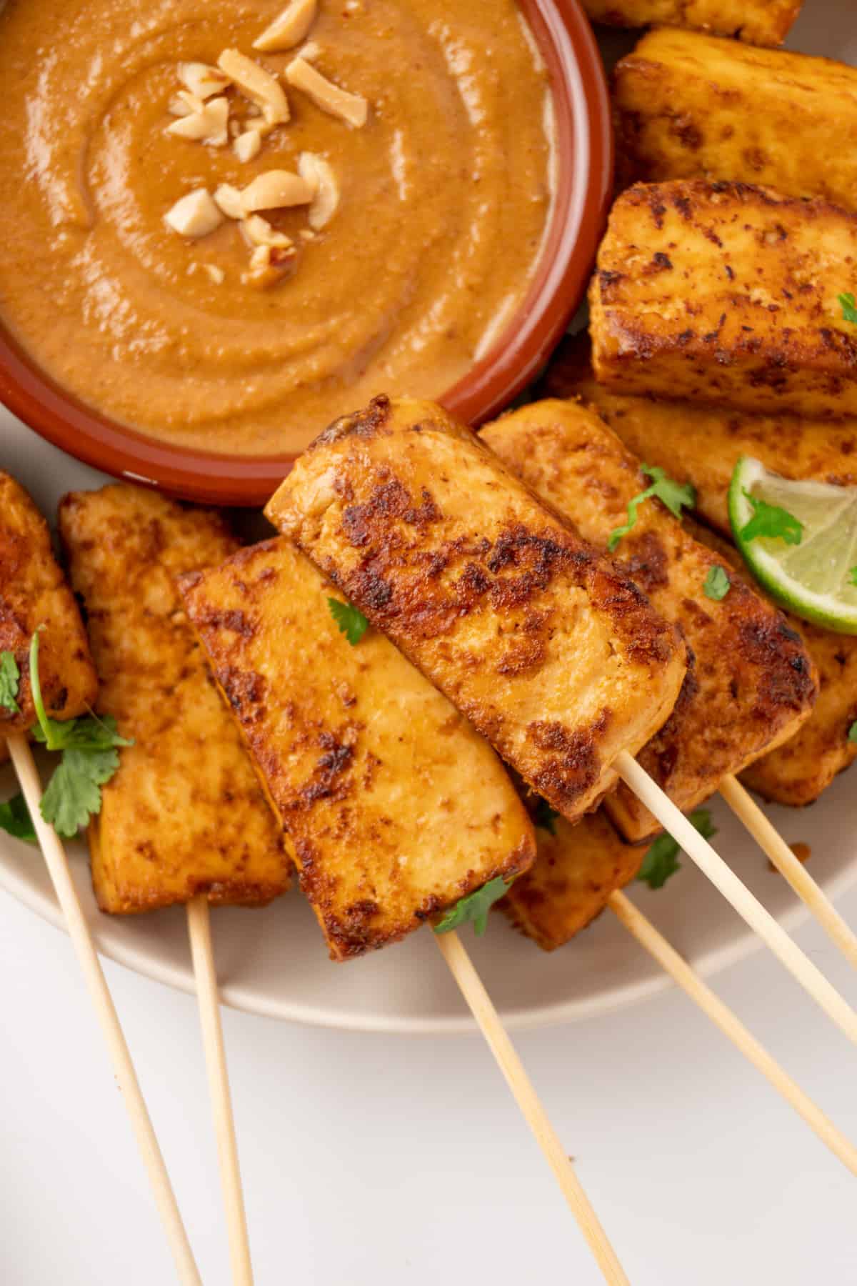 A pile of tofu satay skewers with satay sauce on the side.