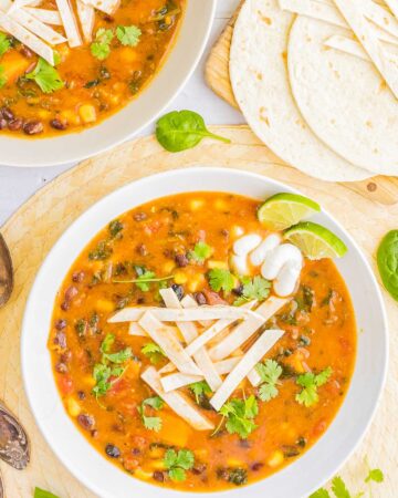 2 white bowls of orange soup loaded with beans, corn, and topped with tortilla strips and freshly chopped cilantro. More tortilla on the side.