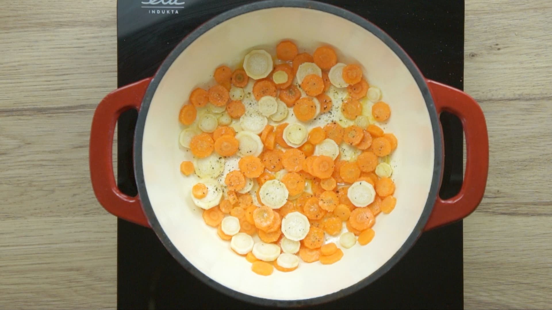 Red enameled Dutch oven with carrot and parsnip slices.