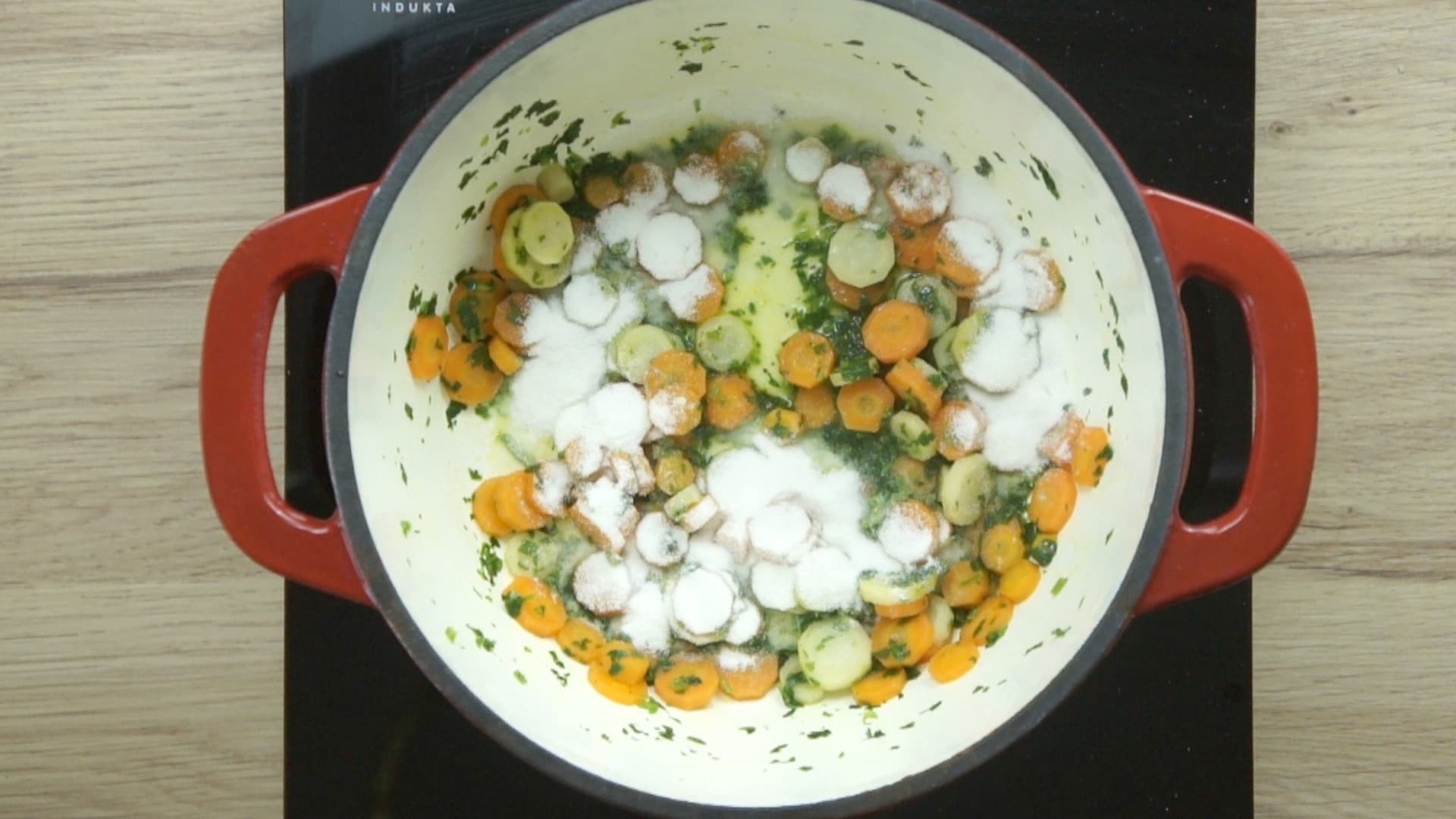 Red enameled Dutch oven with carrot slices, parsnip slices, and freshly chopped green herbs. Sprinkled with white flour.
