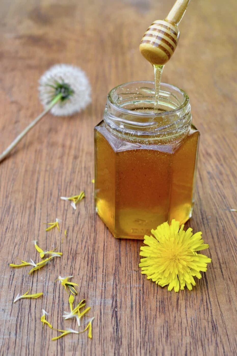 Glass jar with yellow brown syrup with dandelions around it.