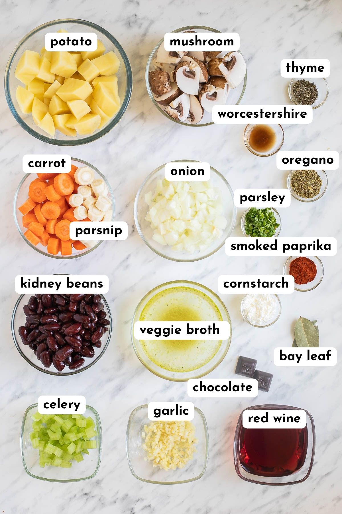 Ingredients of the vegetable stew are is small glass bowls like chopped potatoes, mushrooms, carrots, onion, celery, garlic, red kidney beans, veggie broth, red wine and lots of colorful spices and herbs.