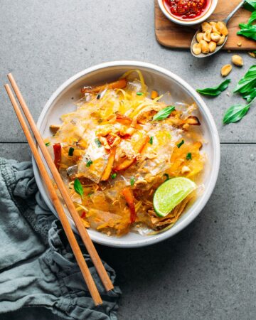 White bowl with rice paper strips, mushrooms, onions in a brown peanut sauce