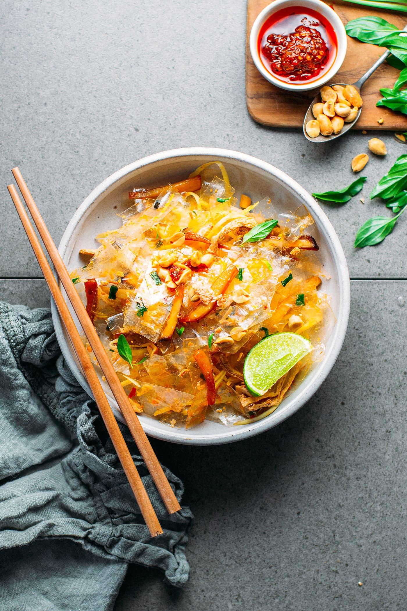 White bowl with rice paper strips, mushrooms, onions in a brown peanut sauce