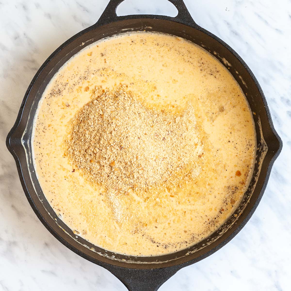A black cast iron skillet from above thin light brown orange creamy sauce with a large heap of yellow flakes in the middle
