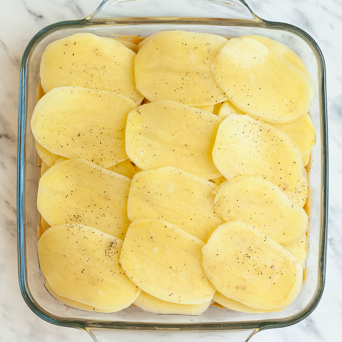 A glass casserole dish with layers of potato slices from above