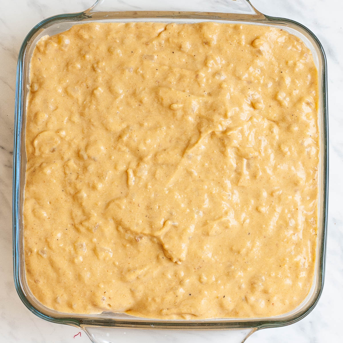 A glass casserole dish from above full of orange creamy sauce.