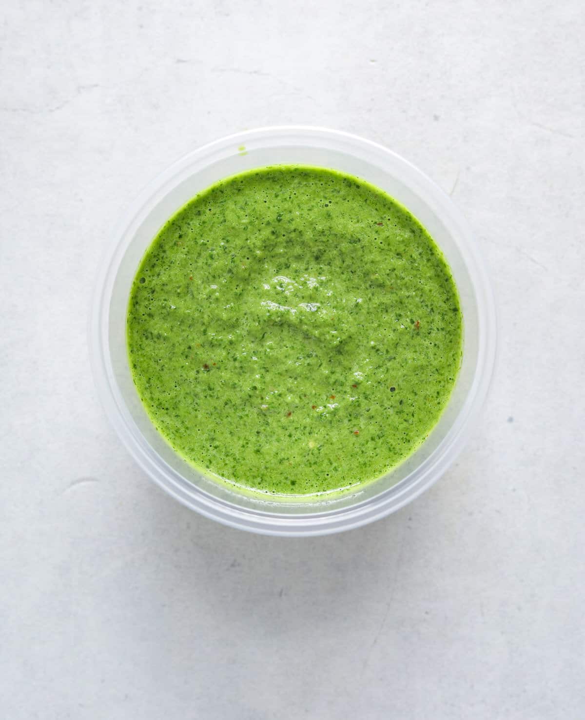 A plastic deli cup filled with vibrant green herbs sauce.