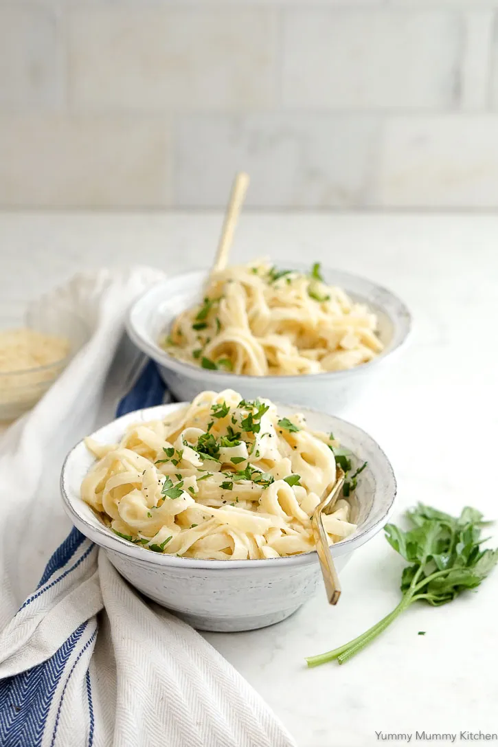 2 bowls of pasta dish with white sauce sprinkled with chopped herbs.