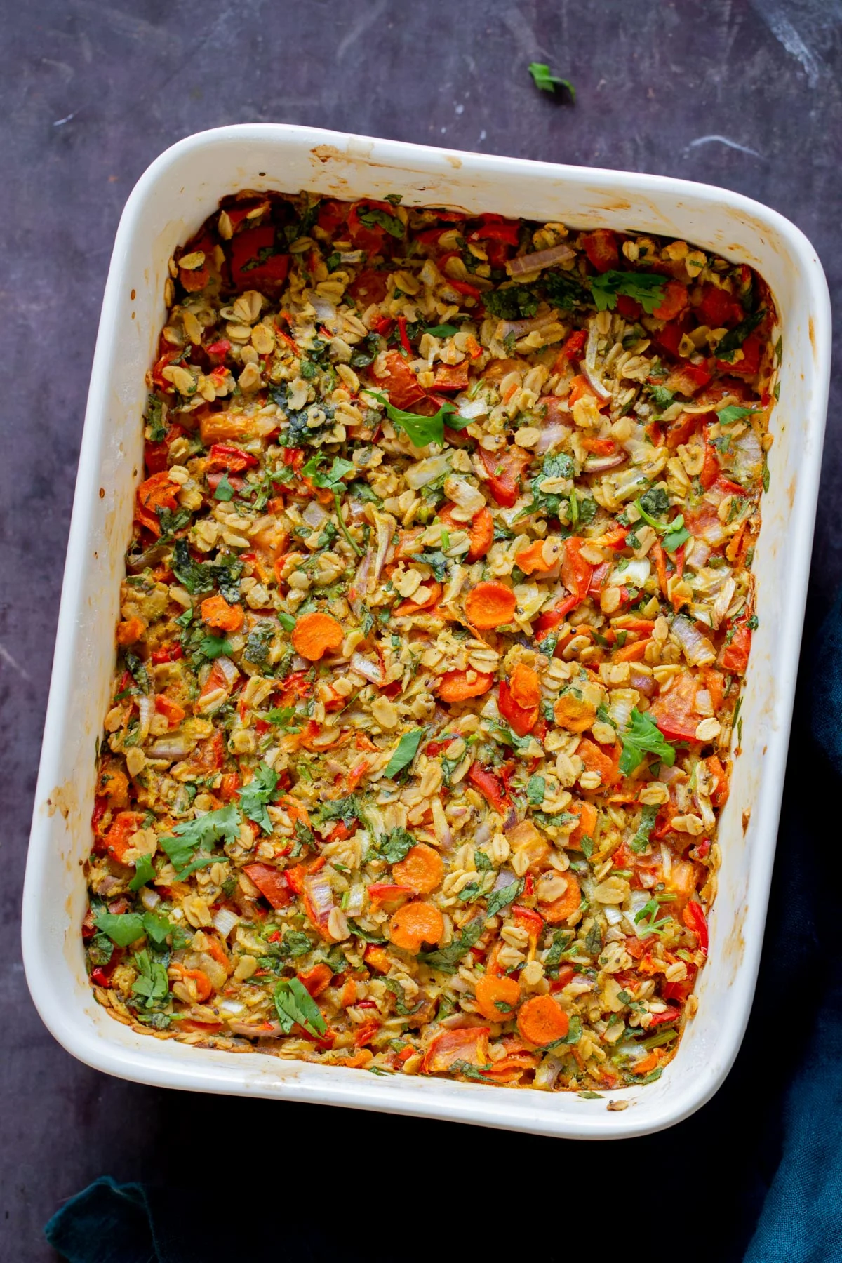 A white casserole with baked oatmeal loaded with vegetables of all colors.
