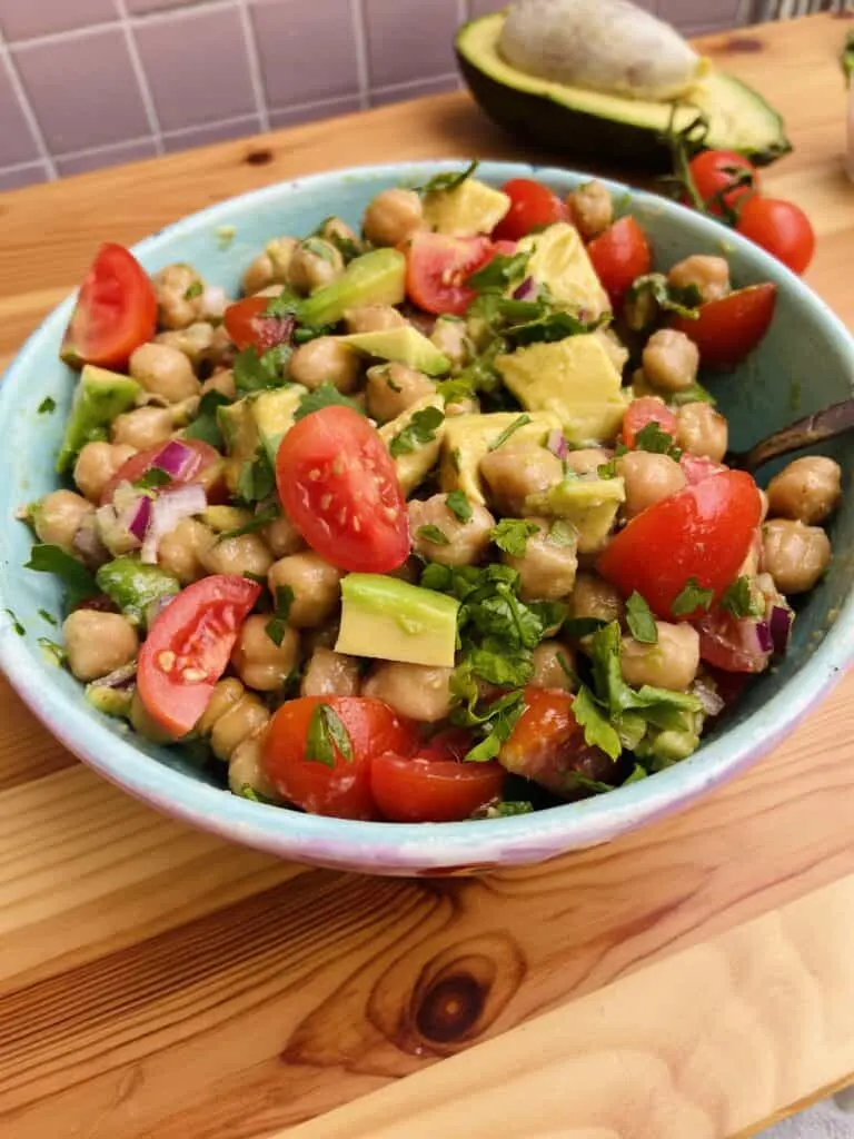 Blue bowl with avocado cubes, cherry tomatoes, chickpeas and chopped green ehrbs