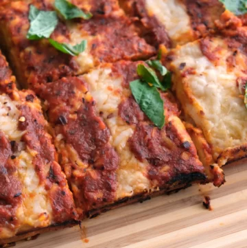 Rectangle pizza sliced into squares topped with red sauce, melted cheese and basil leaves