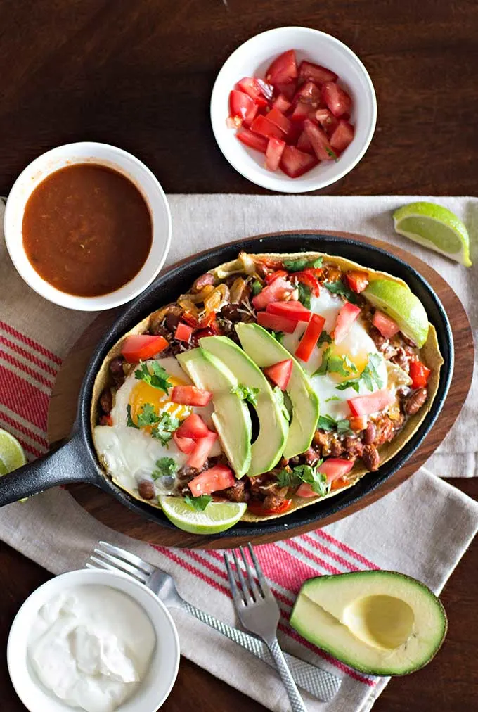Tortilla chips toped with avocado, red pepper, lime, cilantro, chili slices and brown crumbles served in a brown casserole dish