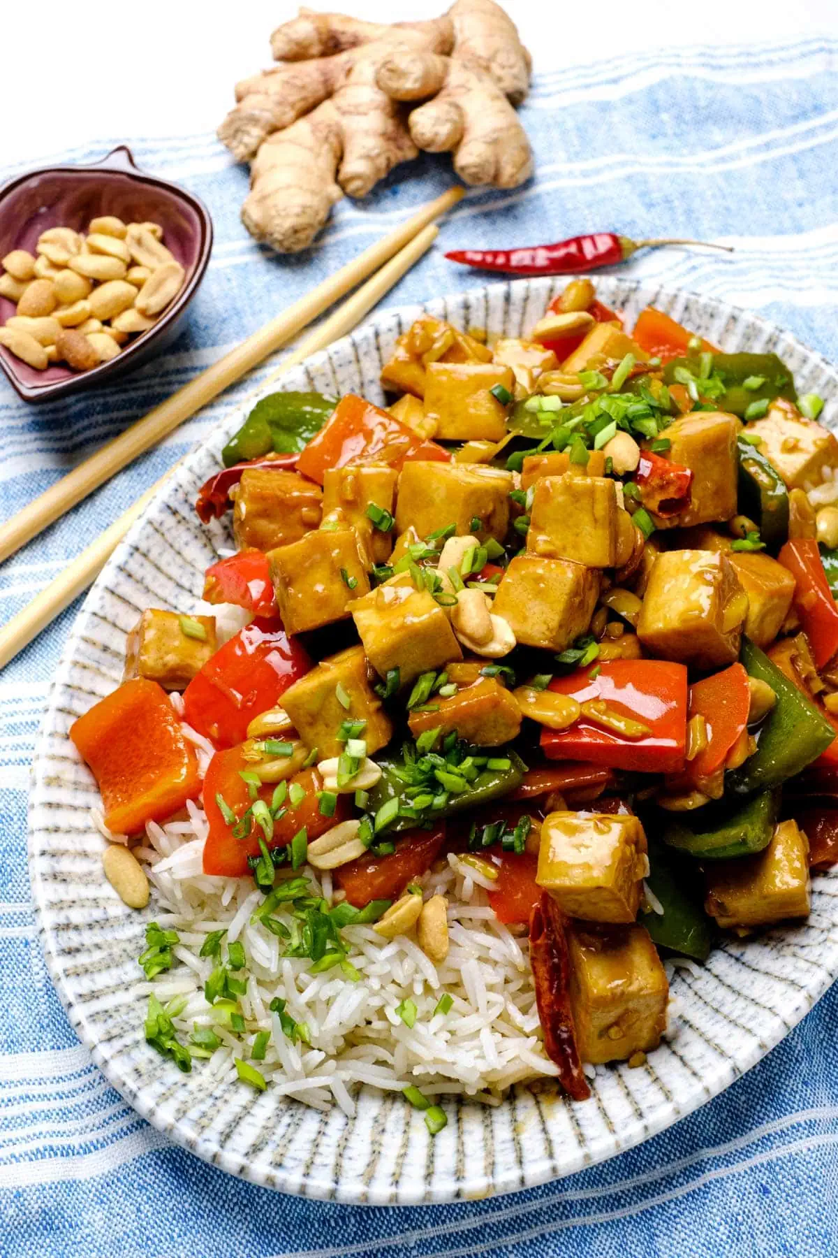 A blue and white plate loaded with rice and topped with bell pepper, tofu cubes, green veggies and chopped scallion.