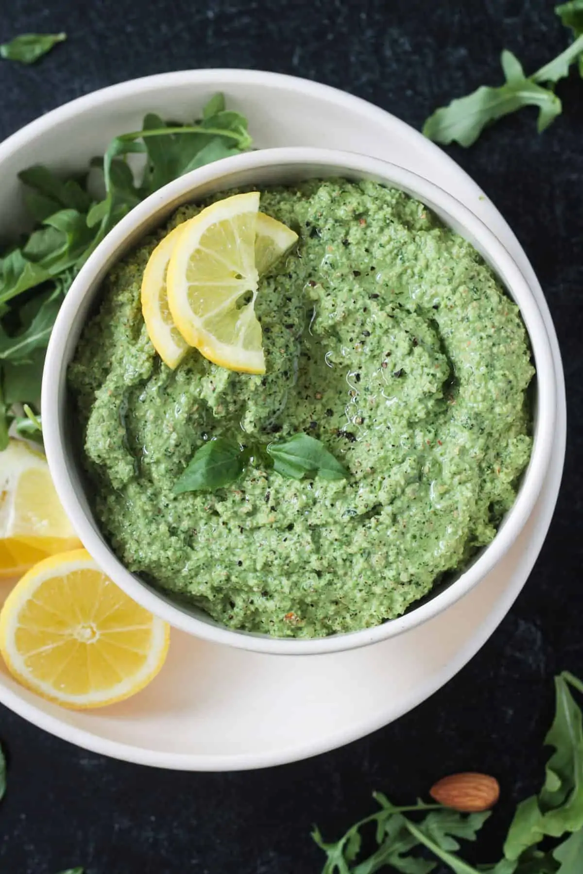 Green pesto sauce in a small bowl topped with lemon slices
