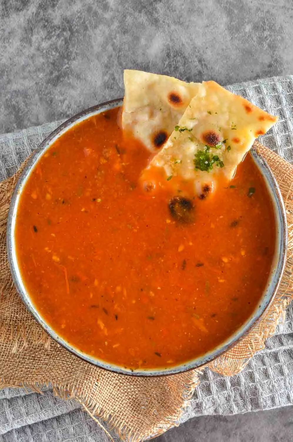 Grey bowl with a red soup. Two naan bread pieces are dipped on the side.
