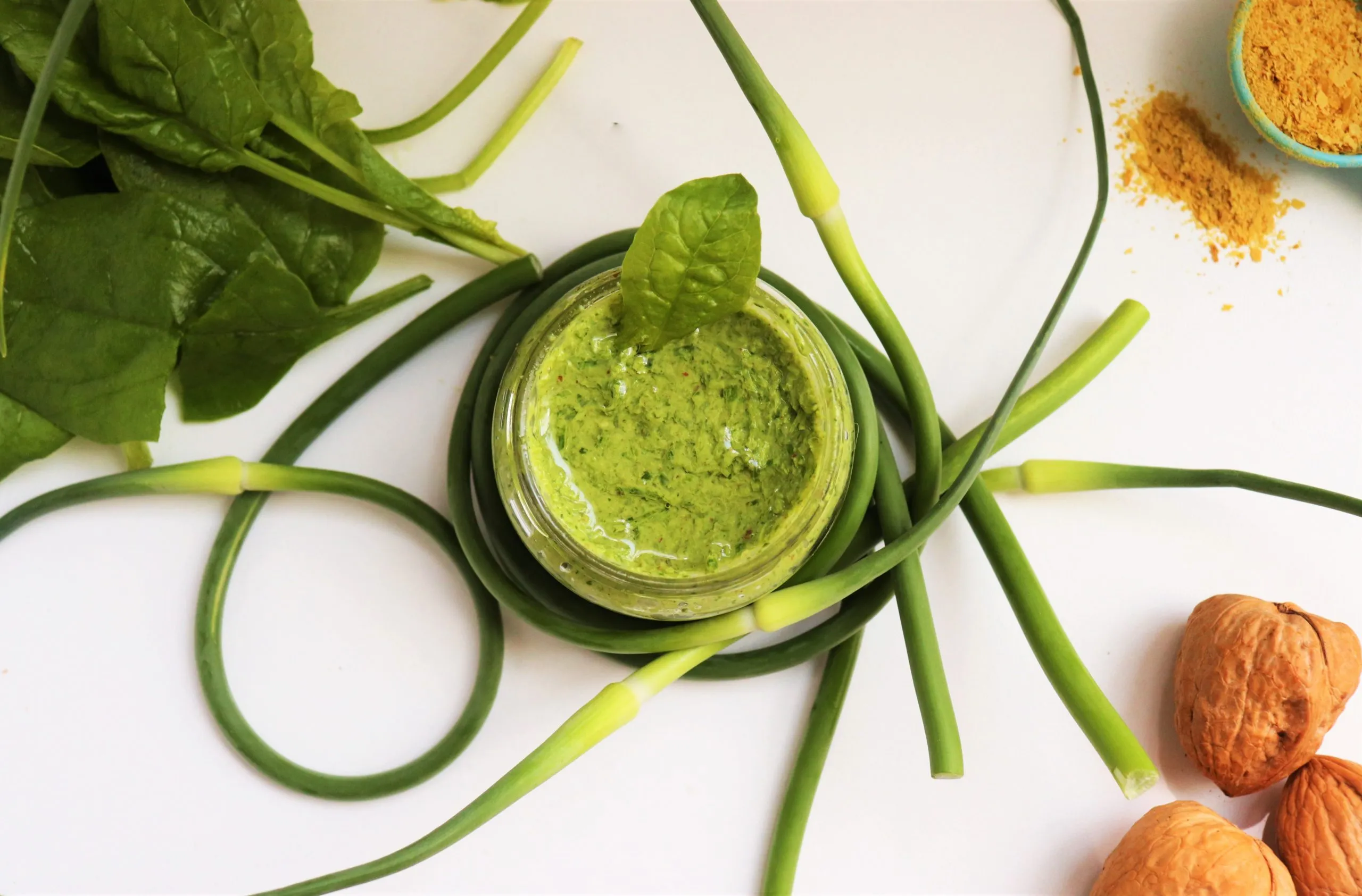 Green pesto sauce in a glass jar with veggie scrapes around it