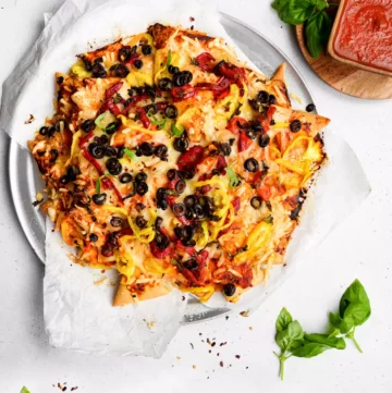 Nachos topped with melted cheese, bell pepper slices, tomato, olives and red sauce.